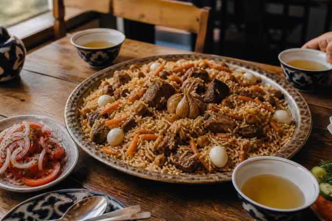 A shared Central Asian table centered on plov, fresh non, achichuk, and tea